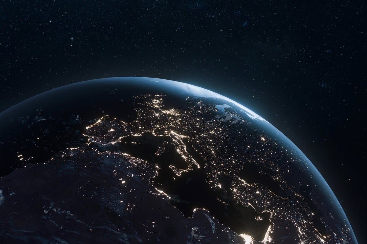 Earth view from space at night with glowing city lights across the continents against the dark starry cosmos