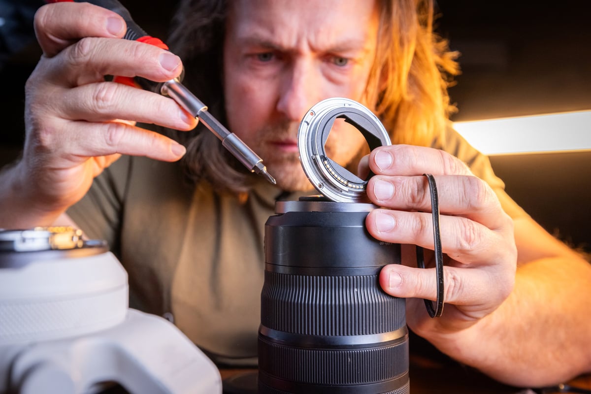 Close-up of a man taking a camera lens apart and holding a weather seal that needs to be replaced