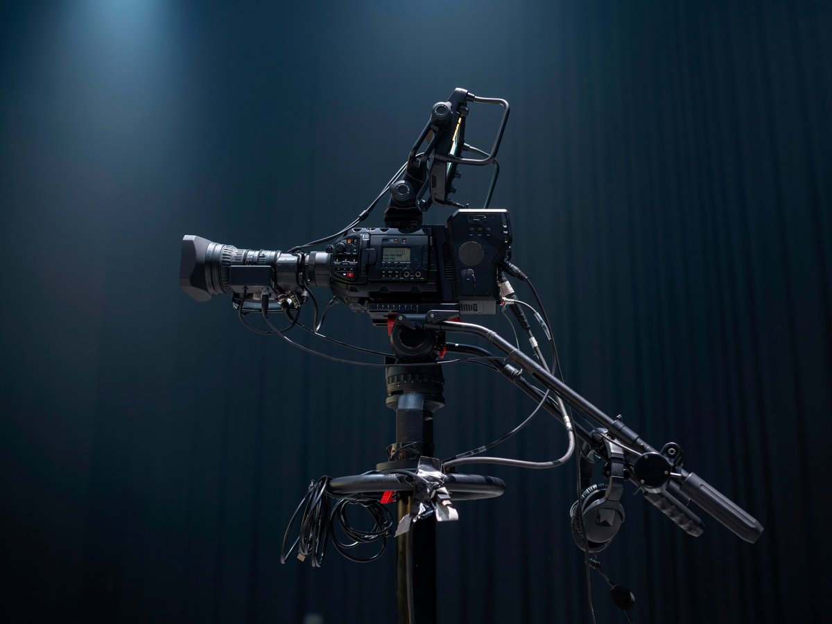 Professional broadcast video camera on a tripod with a blue backdrop in a studio