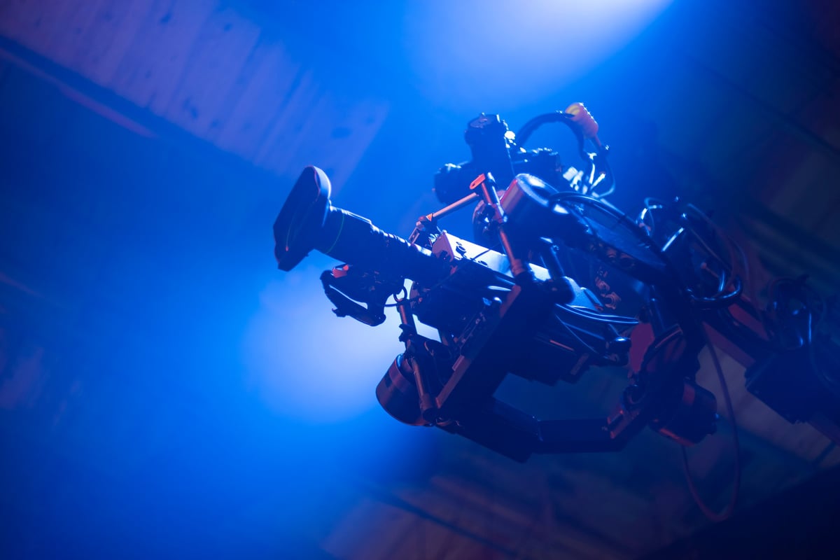 Professional cinema camera mounted on a crane under blue stage lighting in a film studio