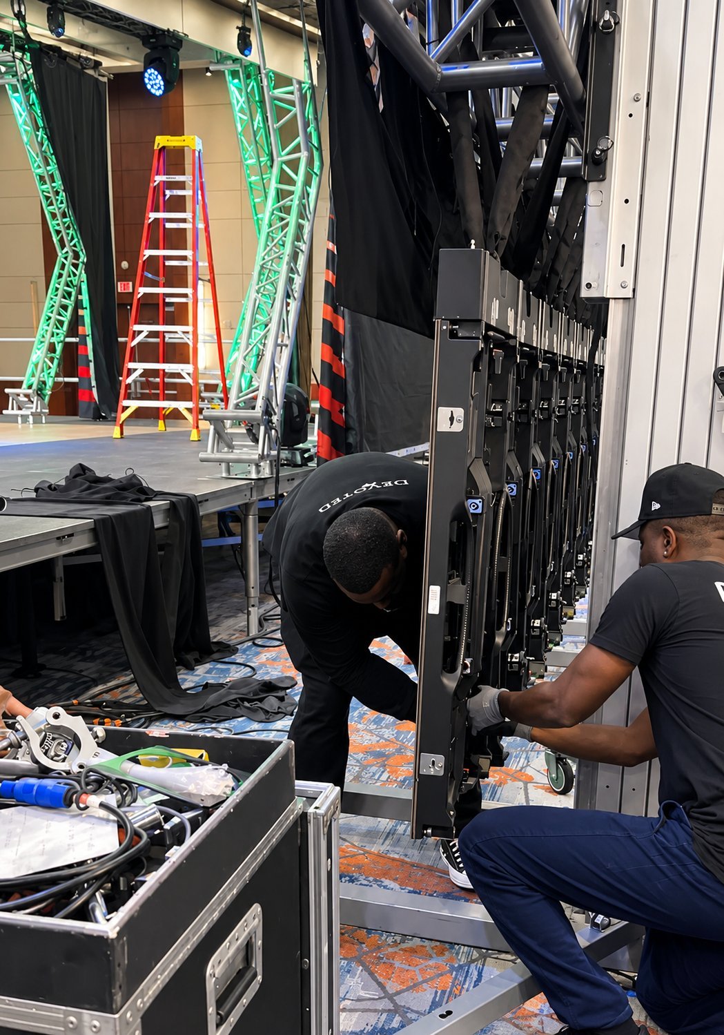 Two technicians working on stage lighting and rigging in a theater warehouse