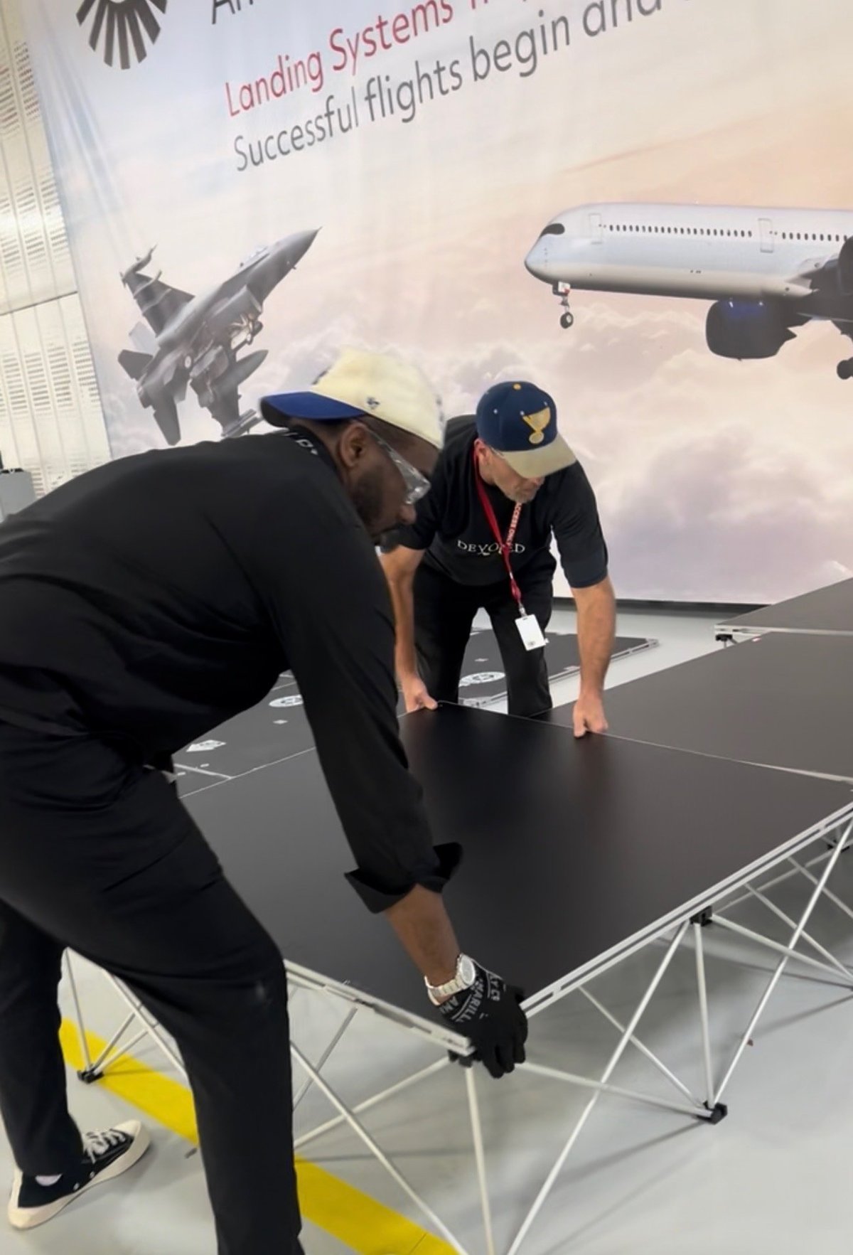 Two DEVOTED crew members staging a black display table at an aviation industry activation event