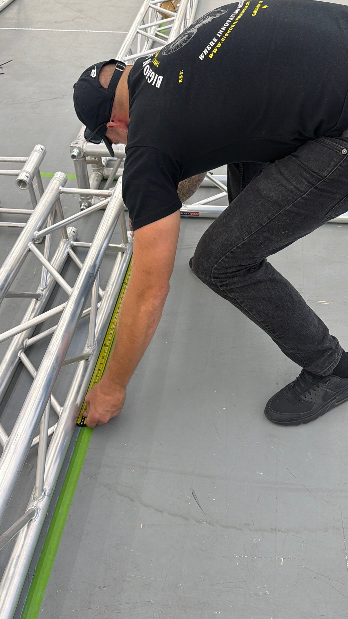 Crew member measuring scaffolding components with a tape measure during staging prep