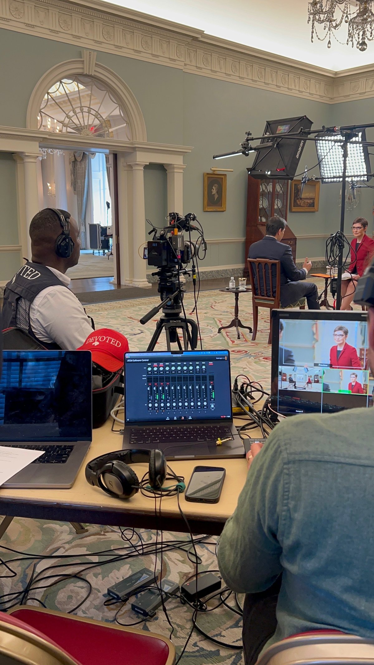 Professional video production setup in an elegant room with crew operating camera and audio equipment while interviewing two people seated in chairs