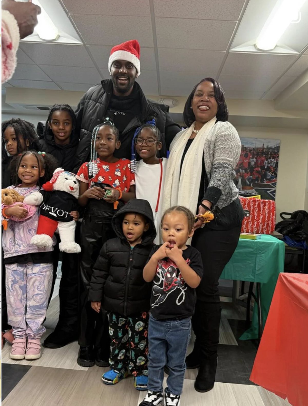 Group of children and adults posing together indoors during a holiday celebration, with decorations and tables visible in the background