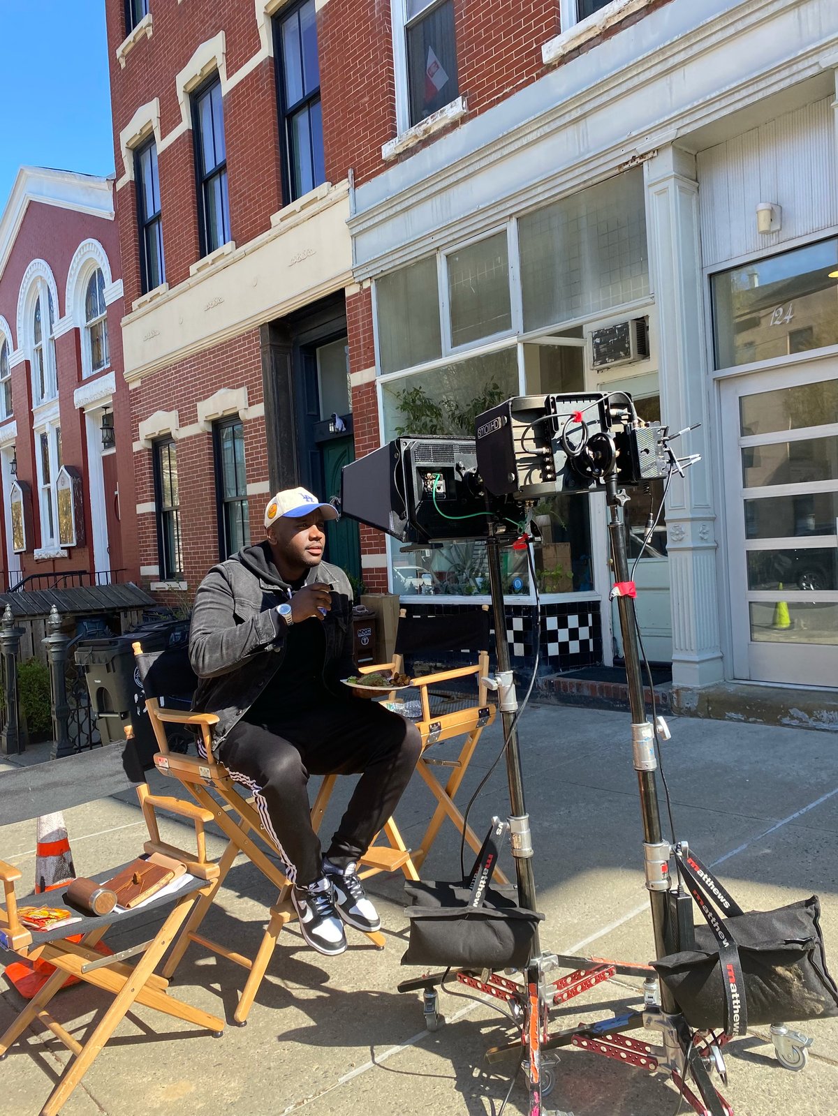 Film director sitting on a canvas chair reviewing footage on a monitor during an outdoor production shoot on a city street