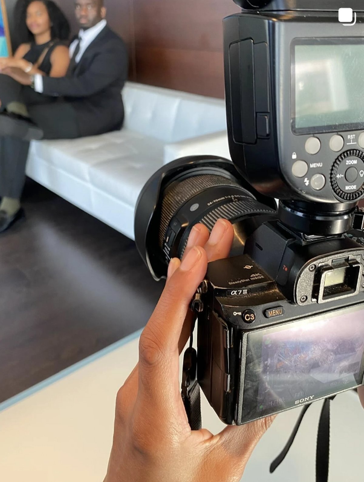 Photographer holding professional camera with flash attachment, capturing couple in business attire in blurred background