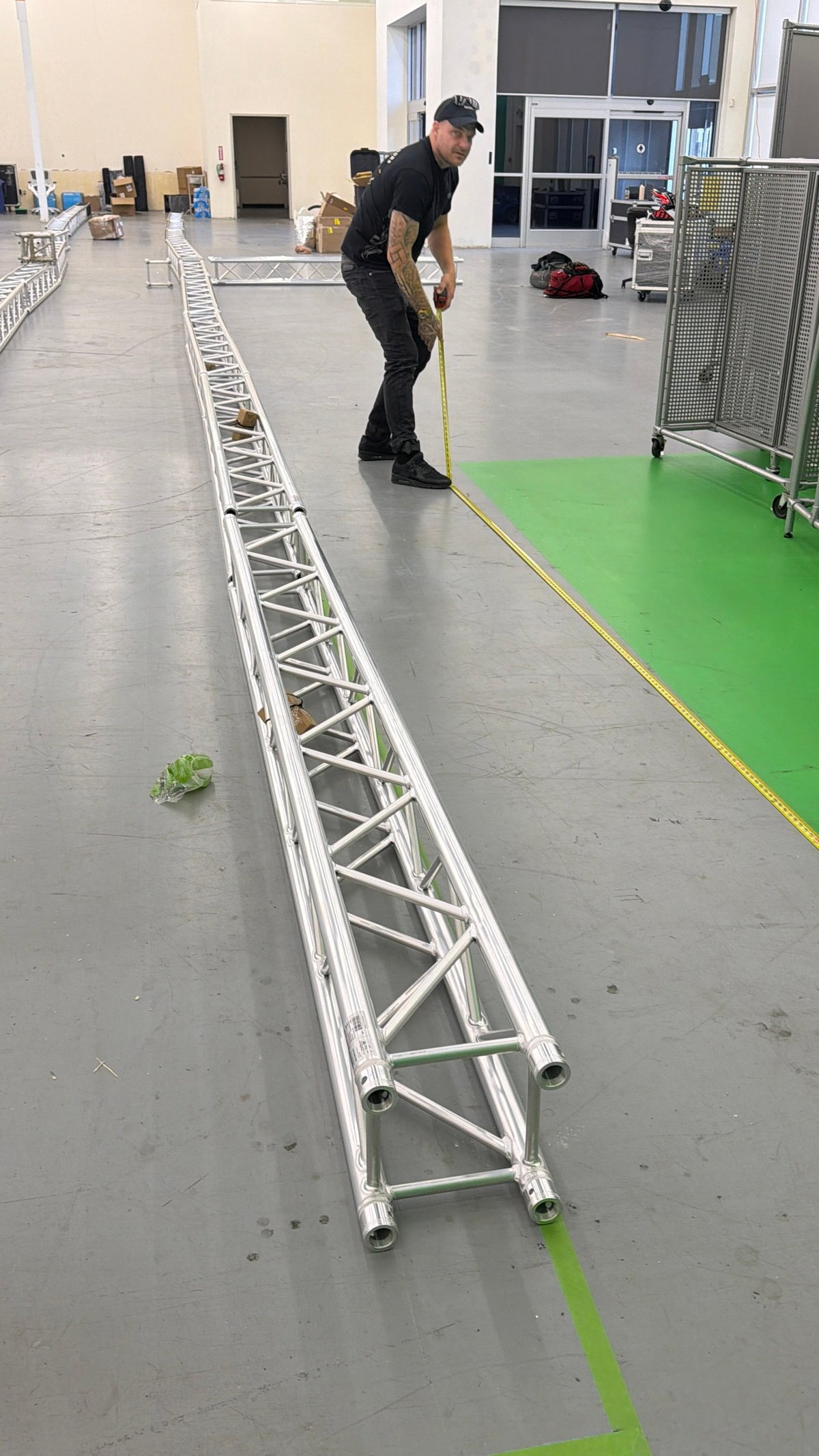 Crew member measuring aluminum truss structure on warehouse floor during event setup