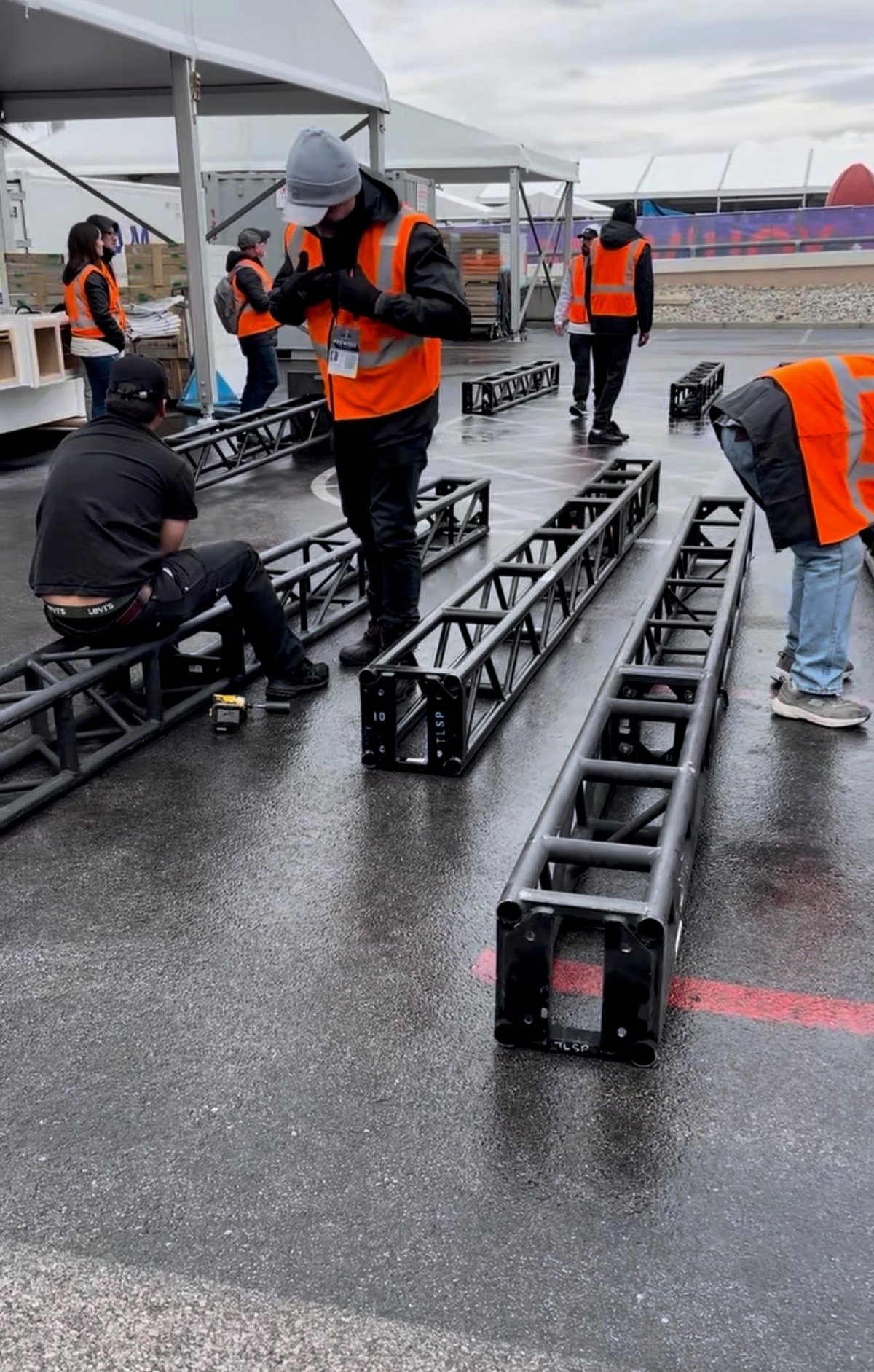 Crew in safety vests assembling metal truss under canopy during outdoor staging