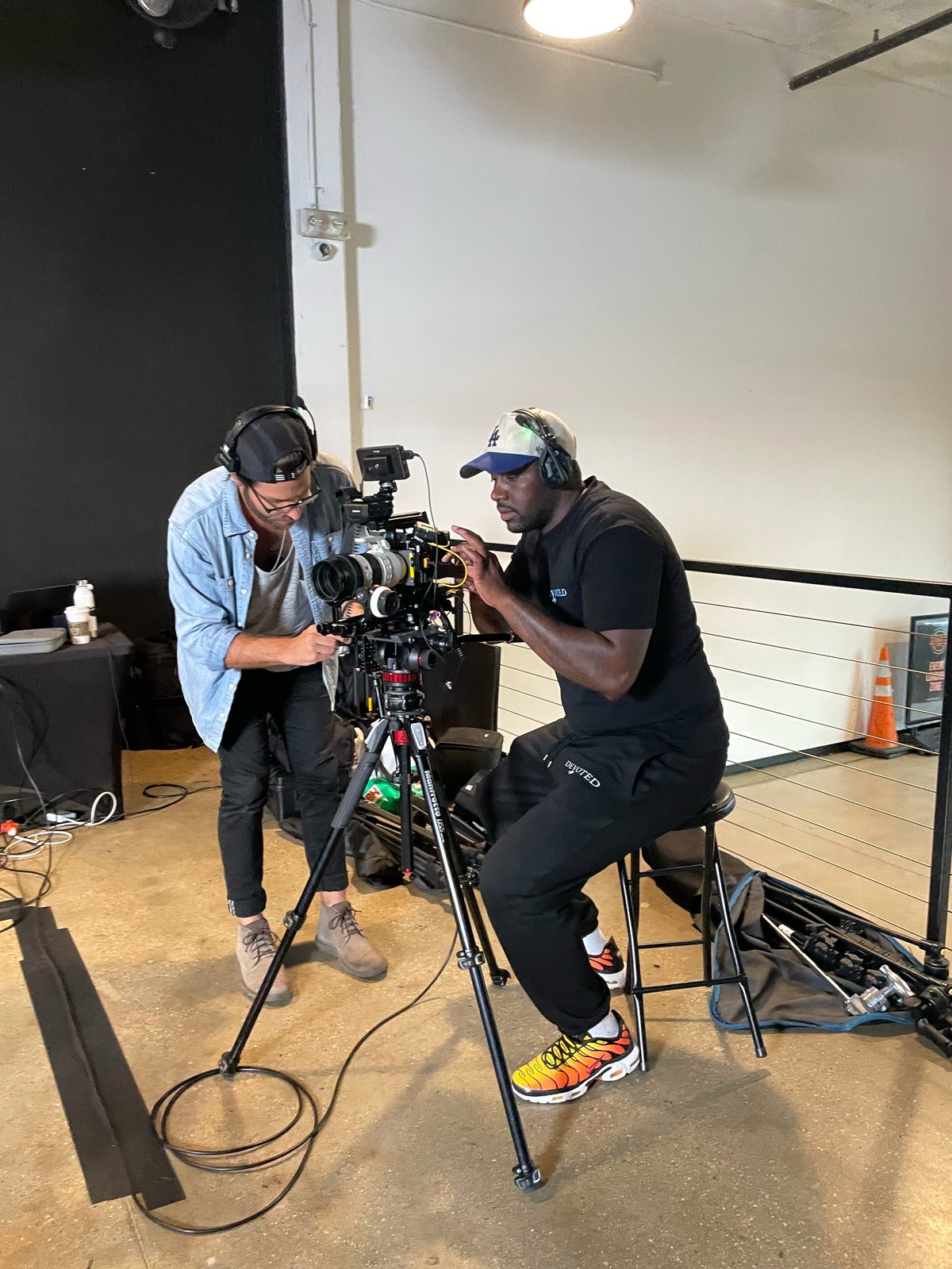 Two cinematographers operating a professional cinema camera on a tripod in a studio with white walls and lighting equipment
