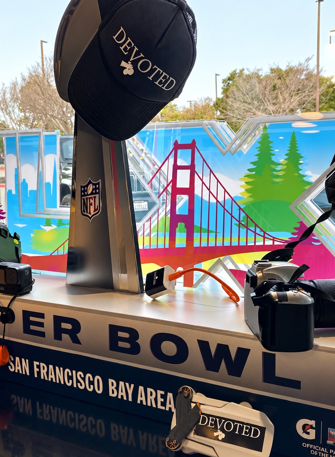 Super Bowl display with large football trophy and Golden Gate Bridge artwork celebrating San Francisco Bay Area, with a DEVOTED branded cap