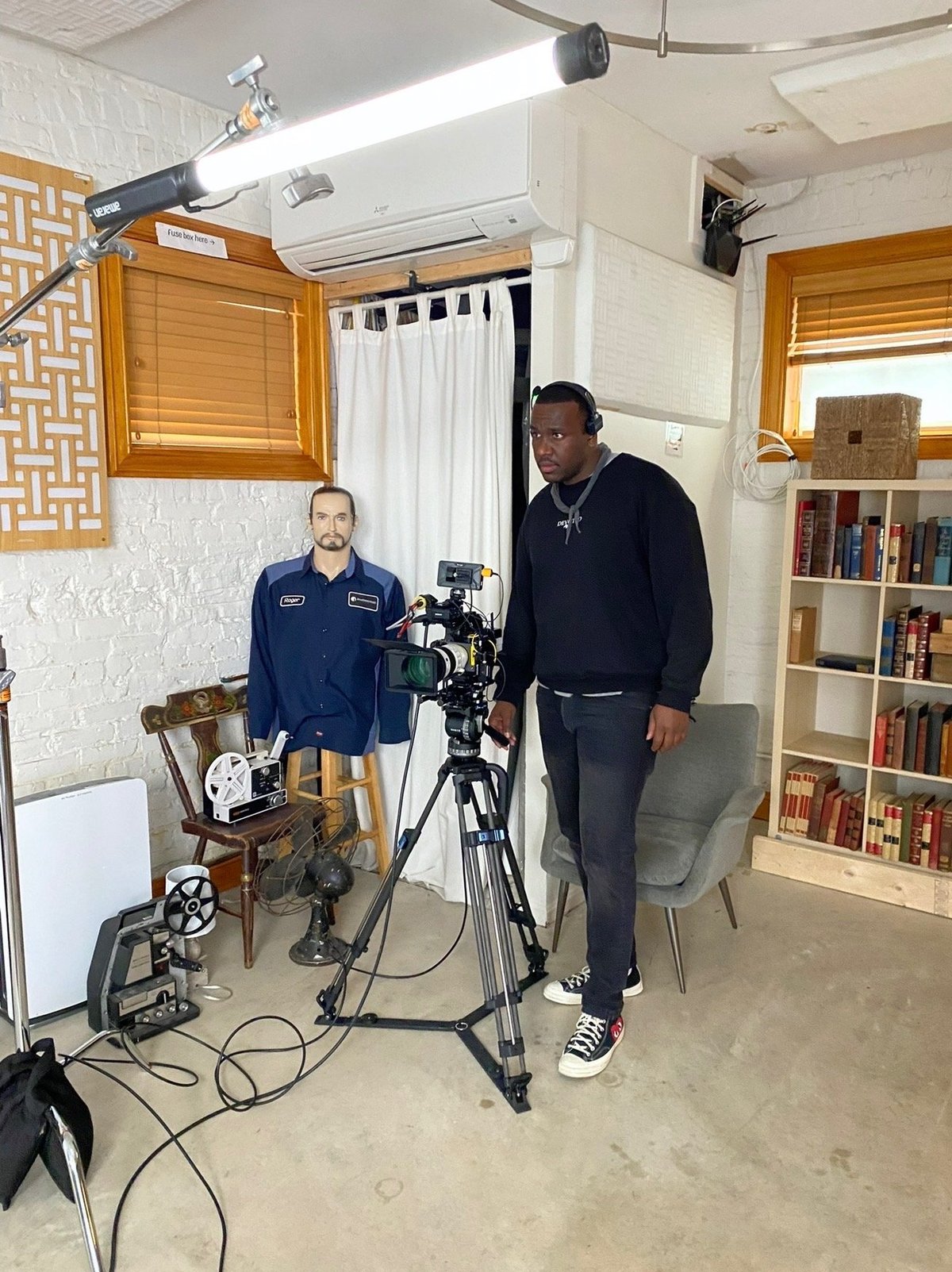 Two men framing up a shot in a home studio with a professional cinema camera on tripod, boom light overhead and a vintage film reel on the table
