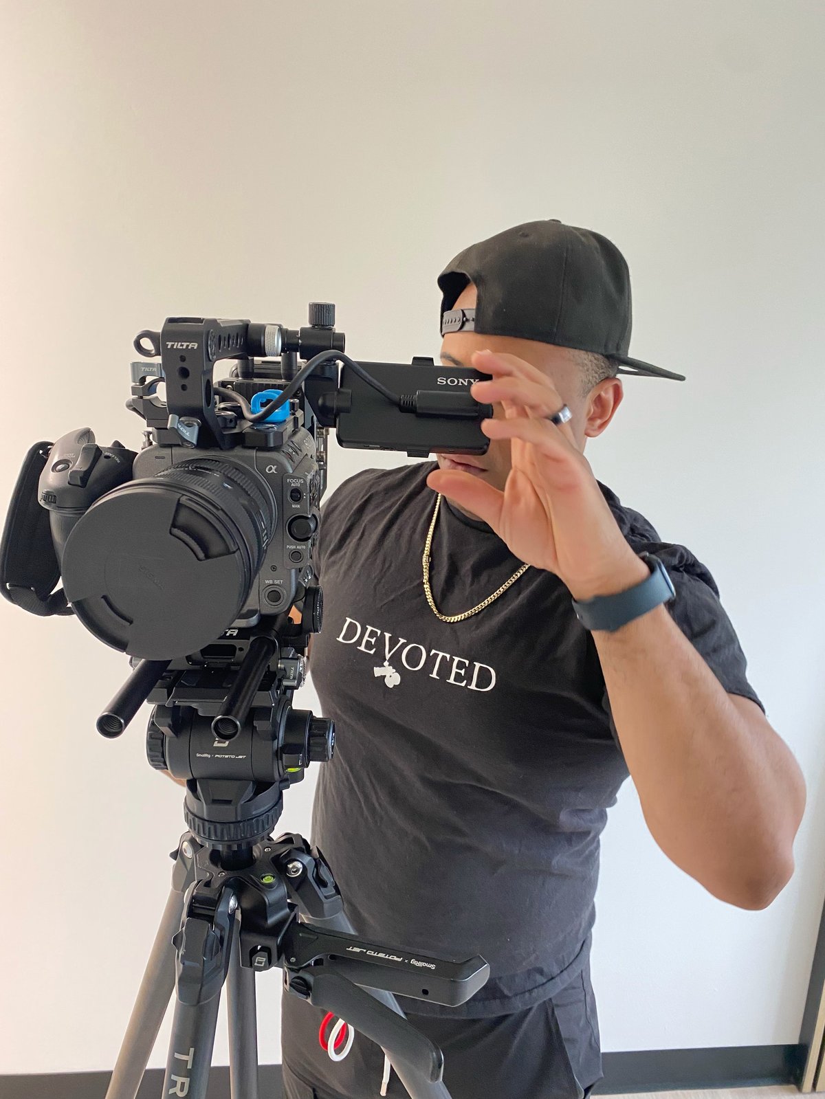 Videographer in black cap and Devoted shirt operating a professional cinema camera on tripod